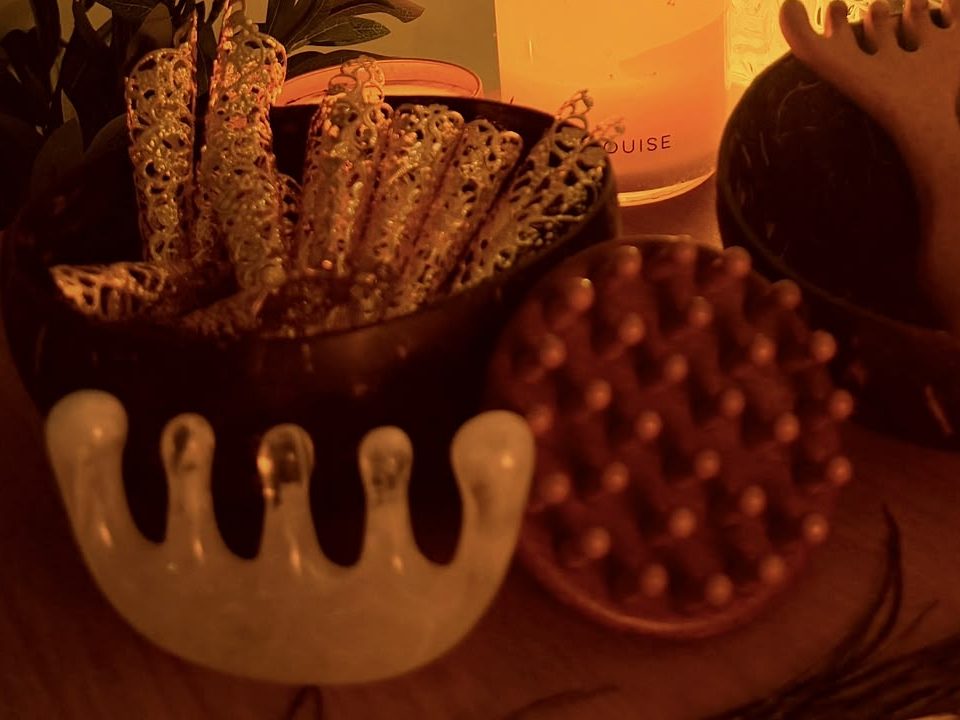 Close-up of filigree scratchers in a coconut bowl, a crystal comb and a soft scalp brush.