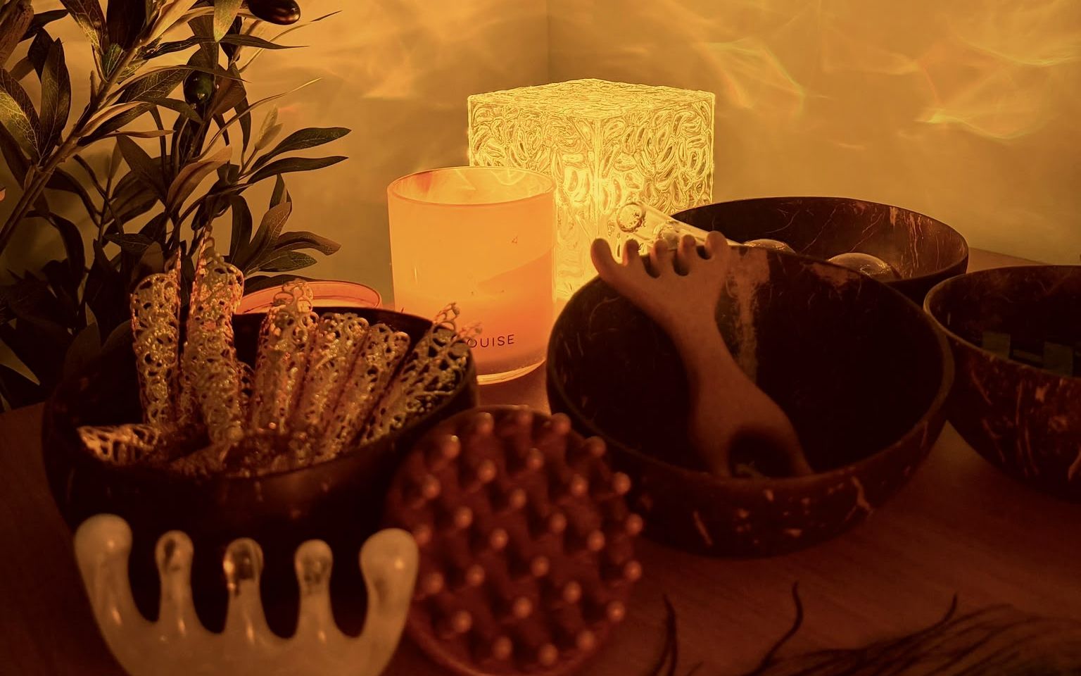 The Scratch Therapy studio by lamplight: a candle and glowing lamp beside coconut bowls of filigree scratchers, a crystal comb and a scalp brush.
